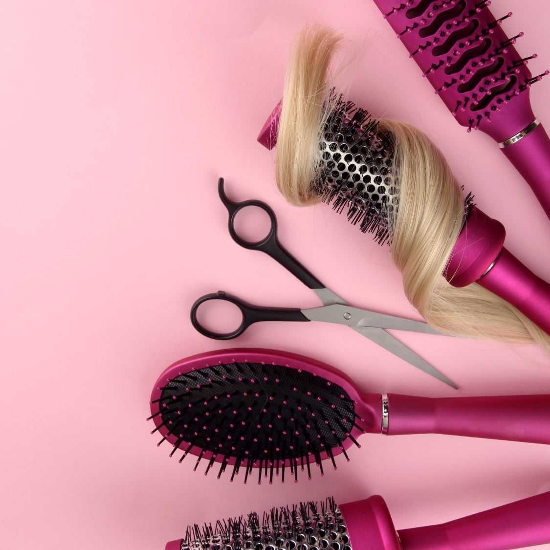 Hair styling tools and a blond hair piece on a pink background.