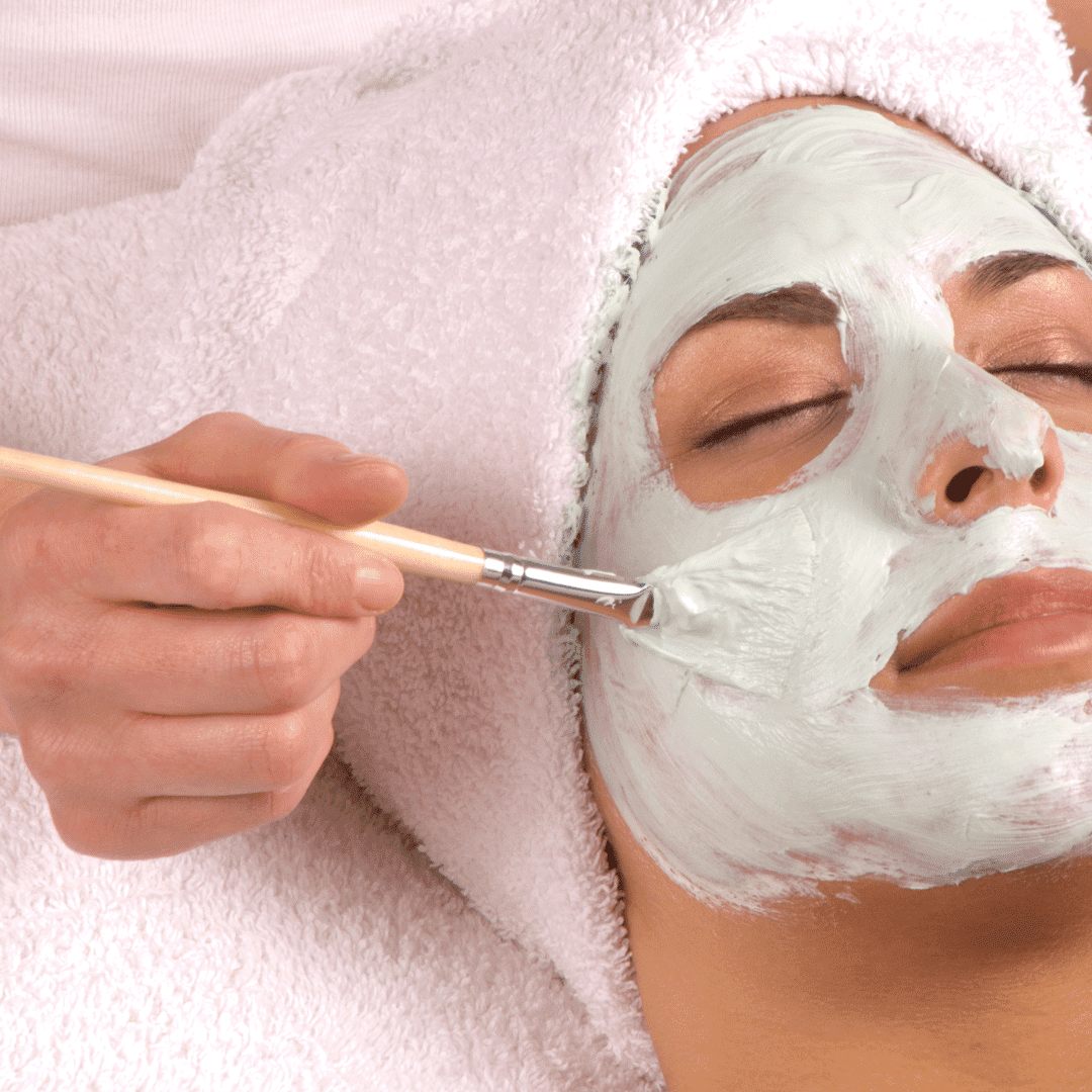 Person receiving a facial treatment, application of a cream mask on their face with a brush.