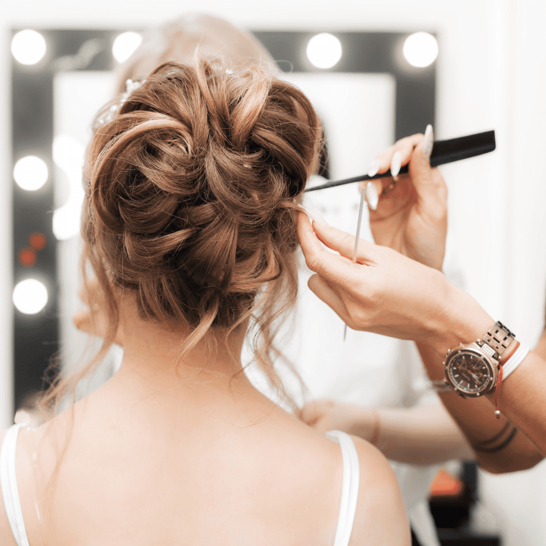 Hair stylist working on an elegant updo for a bride in a well-lit salon with a mirror in the background.
