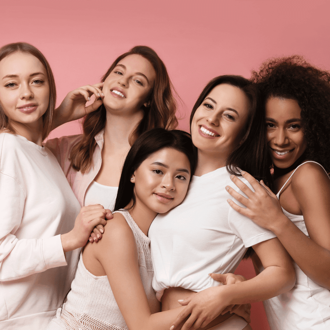 Five women smiling and posing together against a pink background.